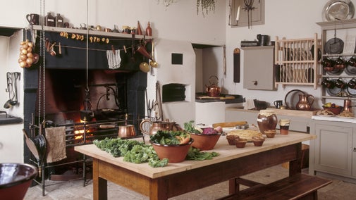 View of the kitchen and fire place where herbs have been brought in to dry and autumn vegetables are being prepared on the table